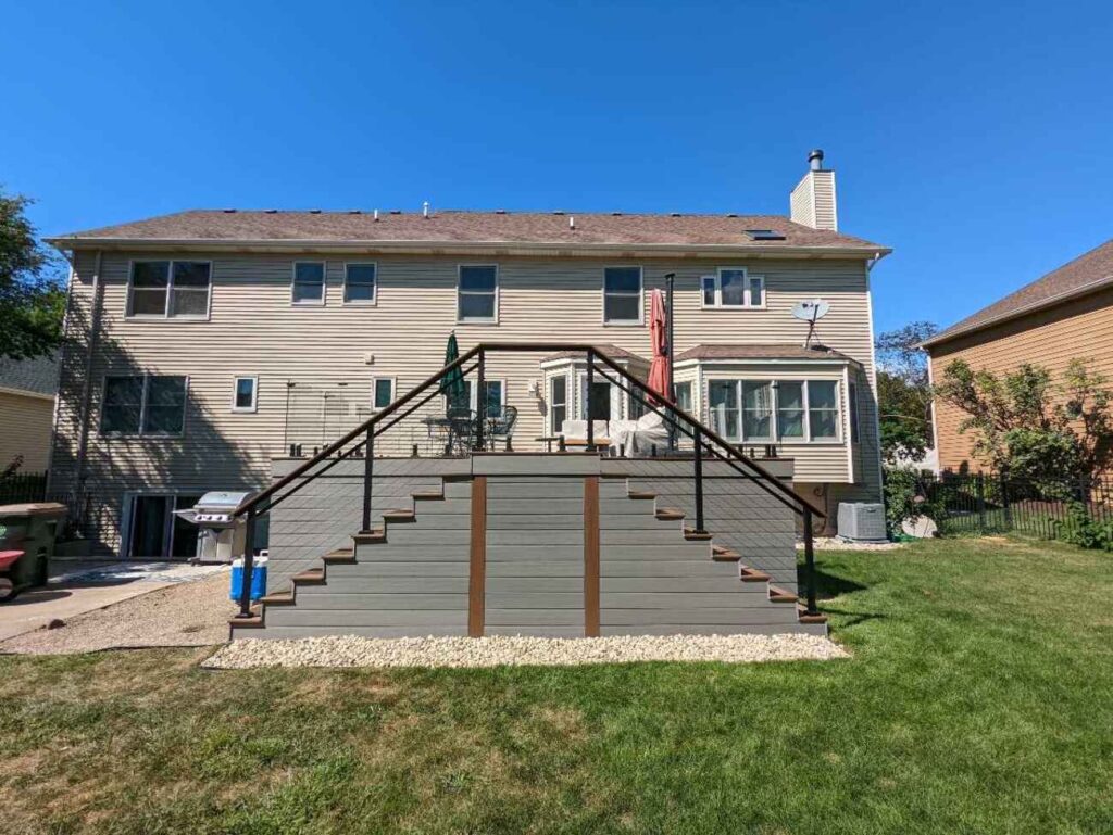 Raised composite deck with glass railing and stairs across the back of a home