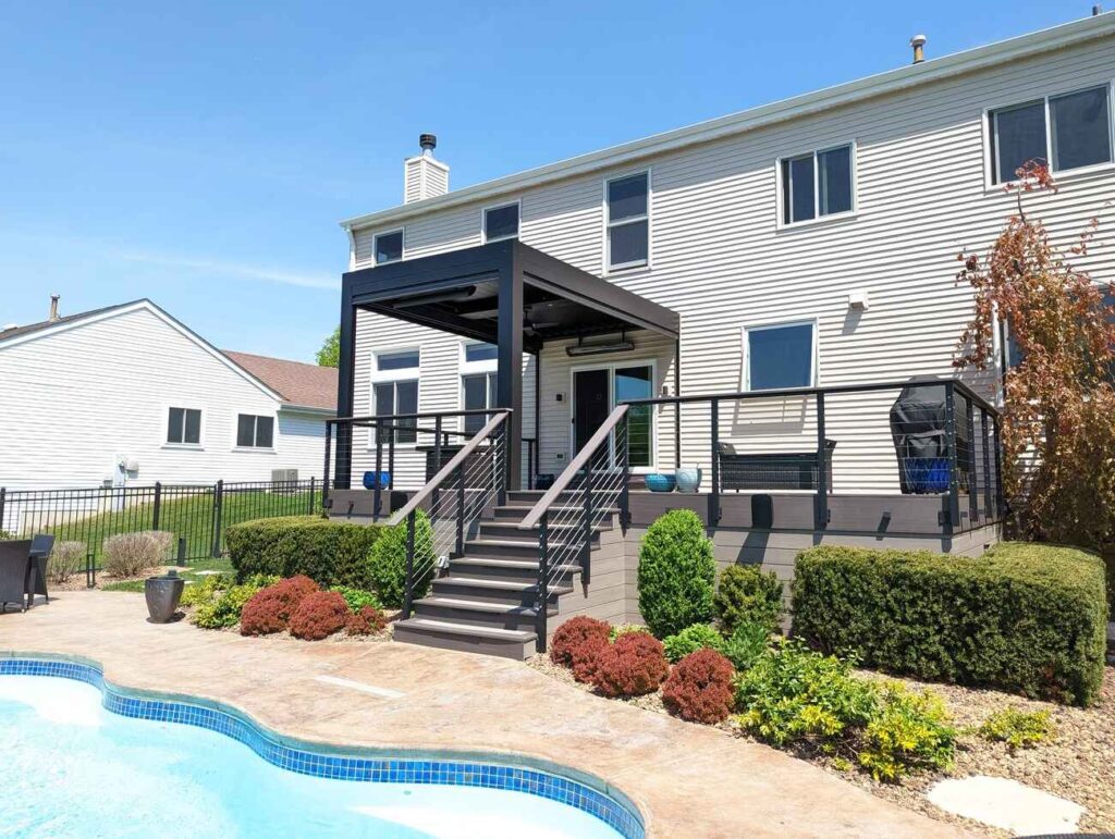 Composite deck with a louvered pergola and cable railing above a backyard pool
