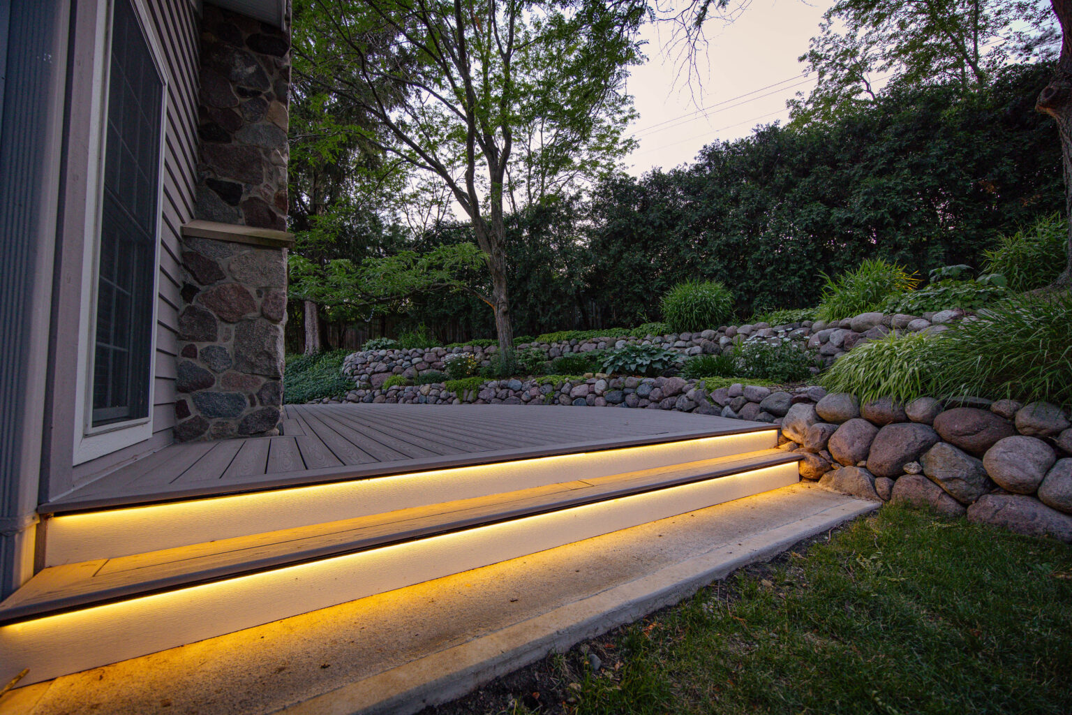 Deck step lighting glowing along a boulder wall